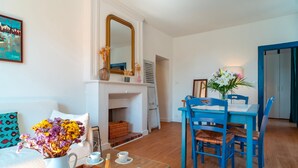 A living room with a white sofa, a glass coffee table, a blue dining table with chairs, a fireplace, and a mirror above it. - Le Closmadeuc - Coeur de ville (Vannes)