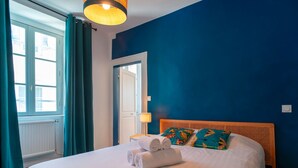 A neatly made bed with rolled towels, a wooden headboard, and colorful pillows. - Le Closmadeuc - Coeur de ville (Vannes)