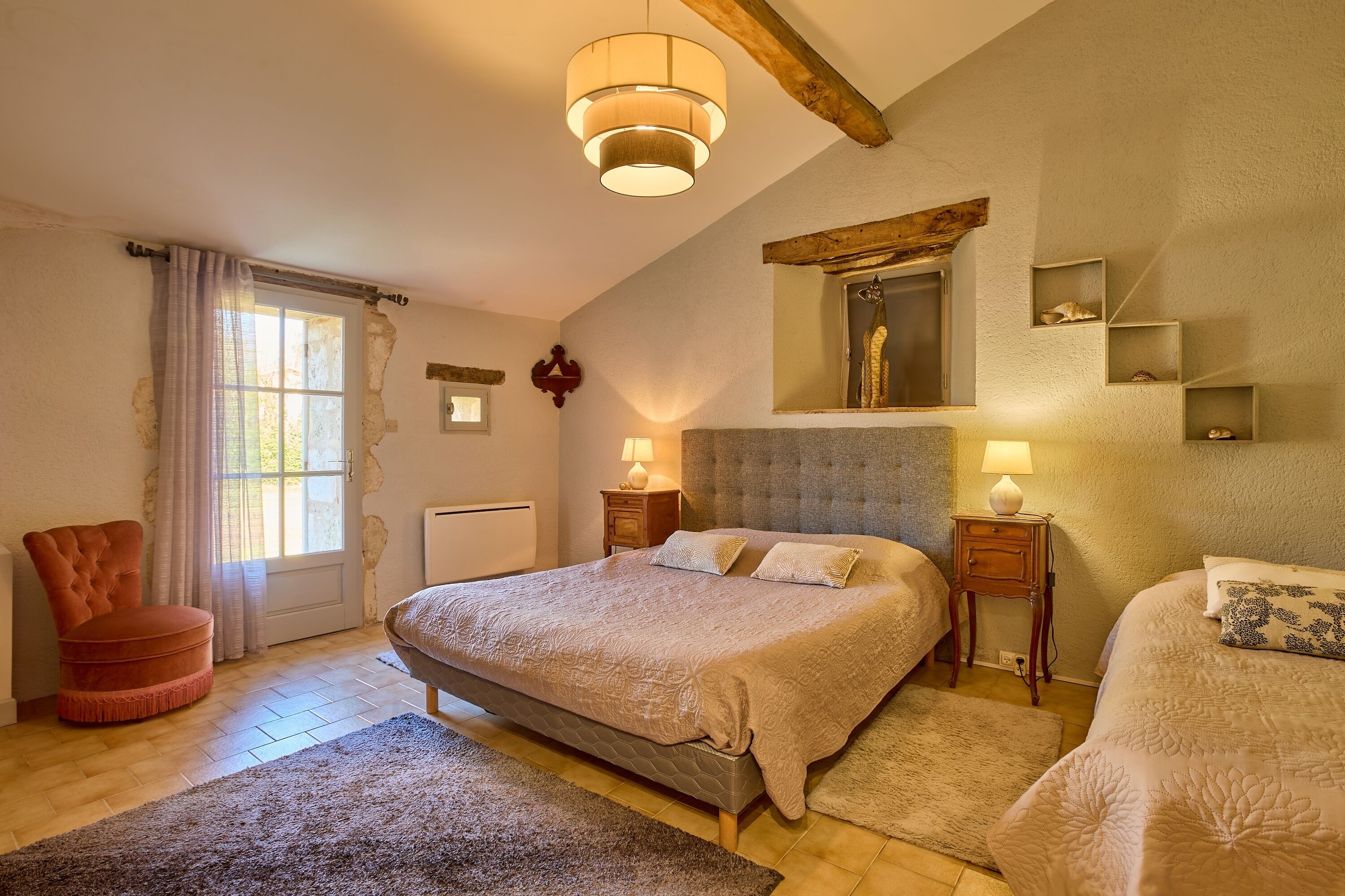 A bedroom with a large bed, two bedside tables, a chair, and a window with curtains.