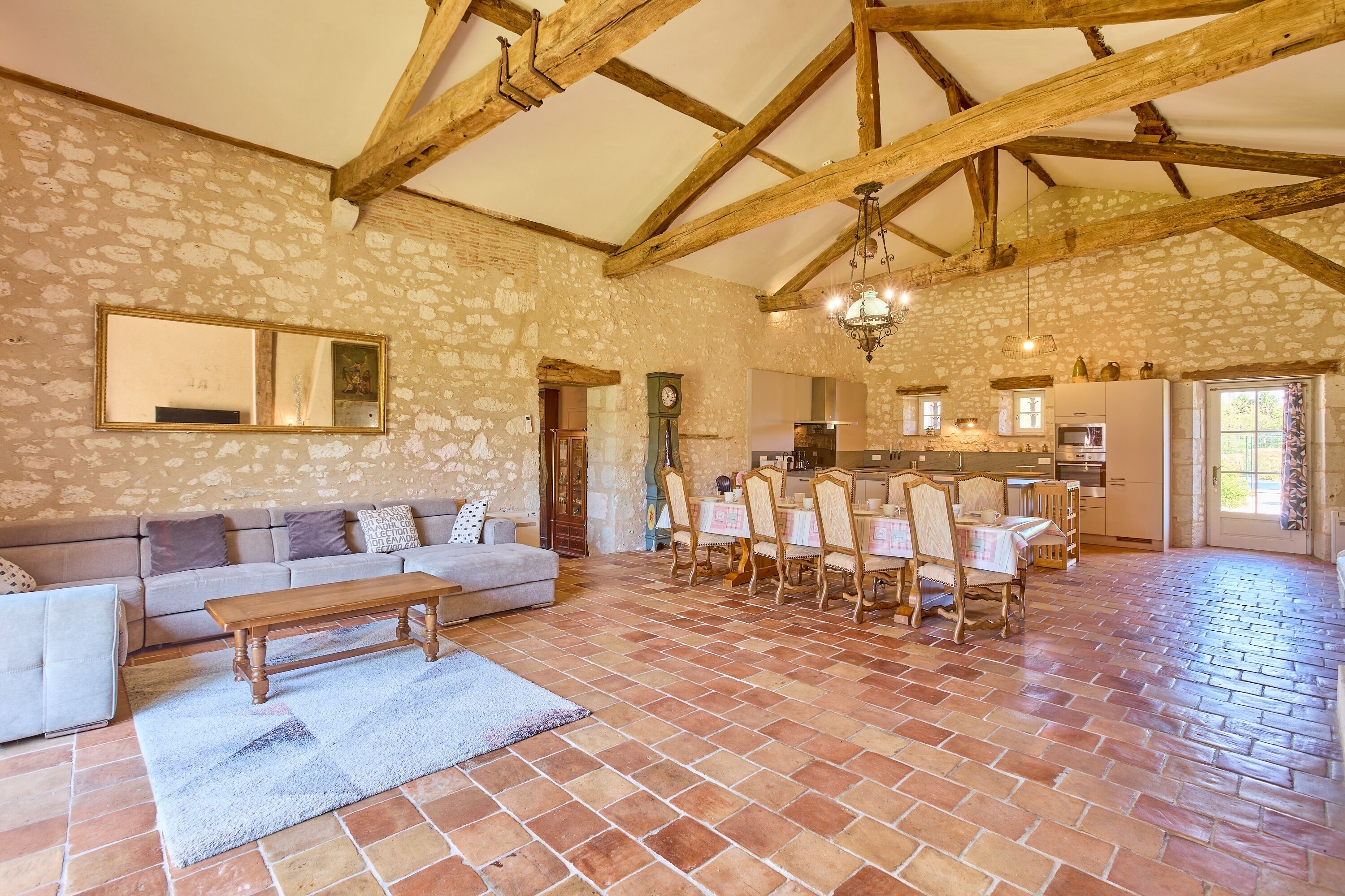 A spacious living area with a stone wall, wooden beams, a dining table with chairs, a sofa, and a coffee table.