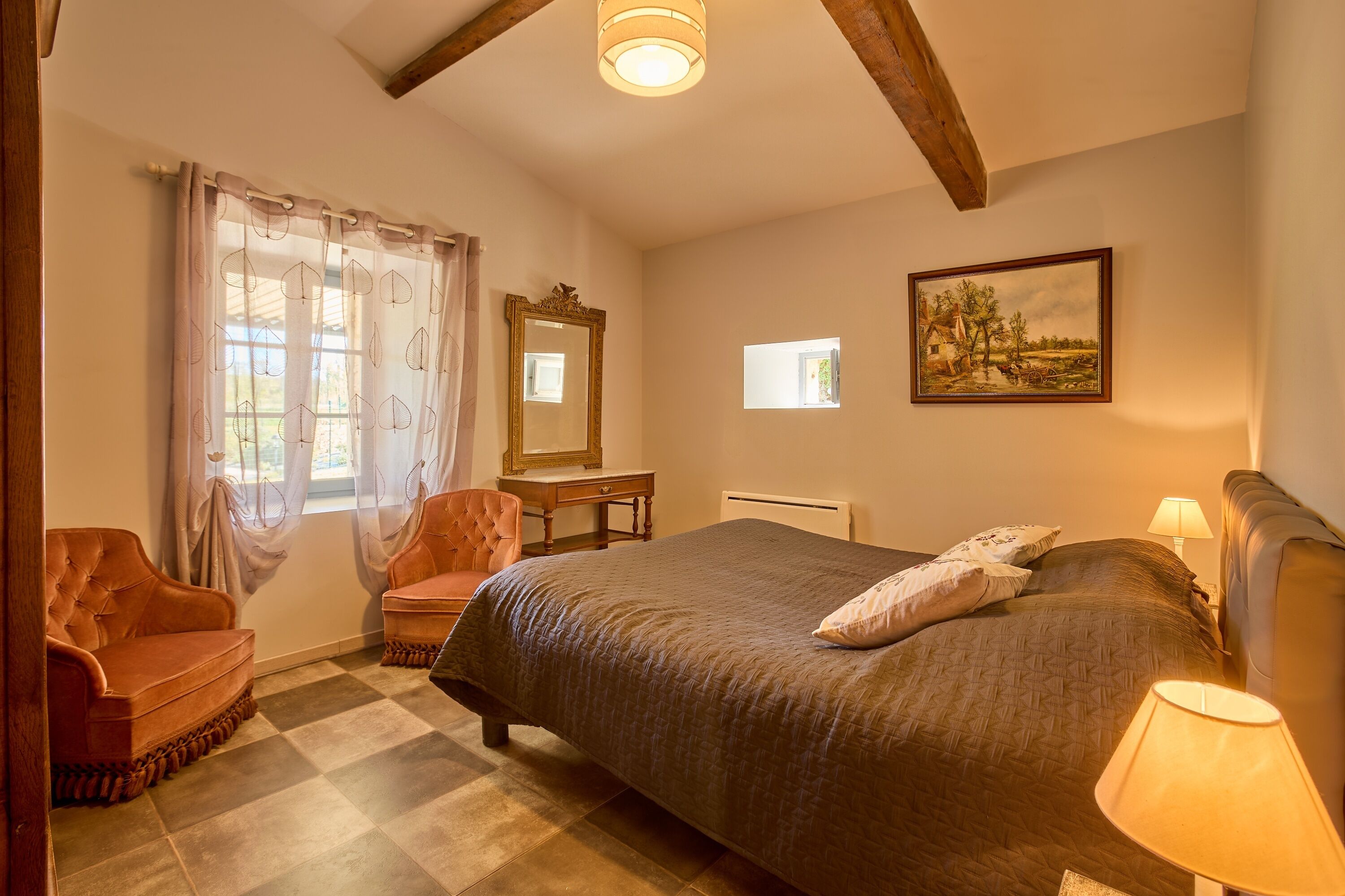 A bedroom with a large bed, a chair, a desk, and a window with curtains.