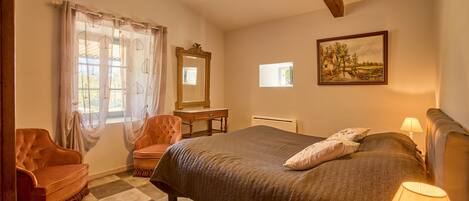 A bedroom with a large bed, a chair, a desk, and a window with curtains.