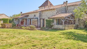 A stone house with a tiled roof, a covered porch, and a grassy yard. - Le Four - Piscine Privée (Thénac)
