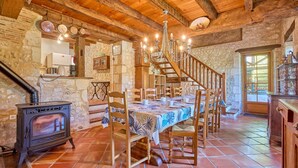 A rustic dining room with a wooden table, chairs, a chandelier, and a stone wall. - Le Four - Piscine Privée (Thénac)