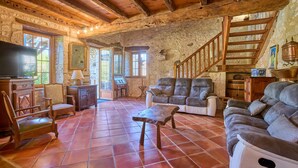 A rustic living room with wooden beams, a stone wall, a sofa, a coffee table, and a staircase. - Le Four - Piscine Privée (Thénac)