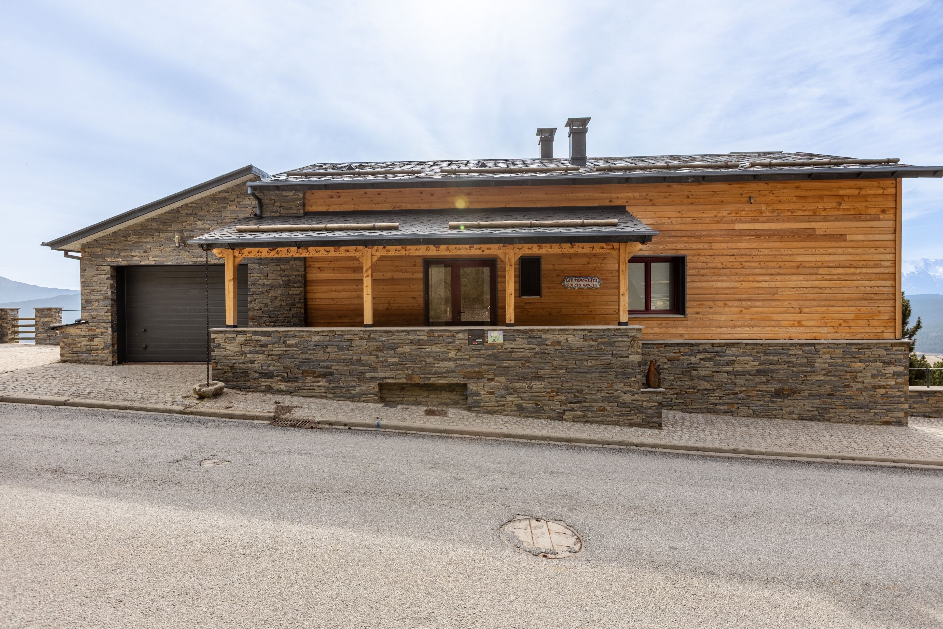 A modern wooden house with a stone foundation, a garage, and a view of the mountains.
