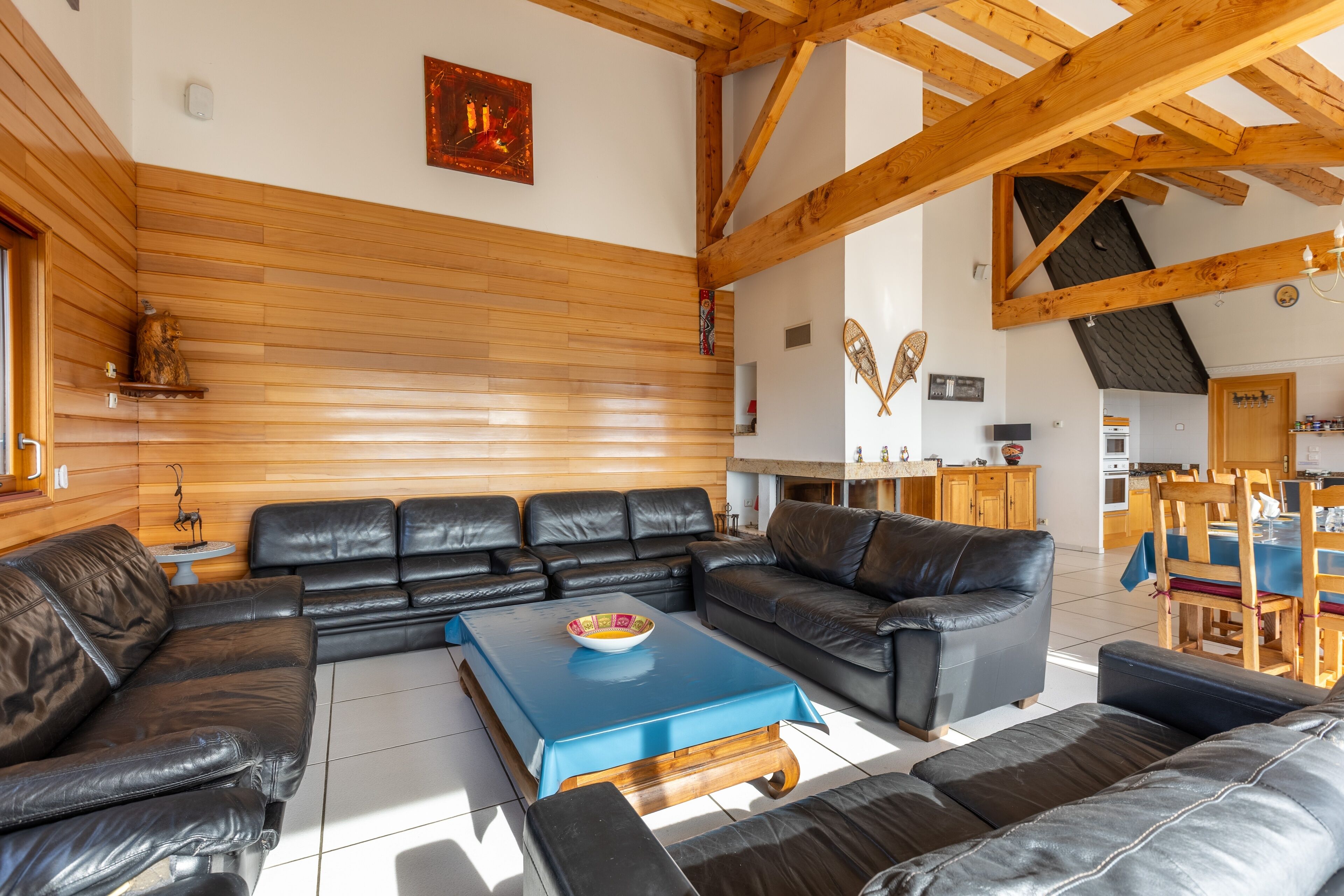 A spacious living area with a large L-shaped black leather sofa set, a blue coffee table, and wooden paneling on the walls.