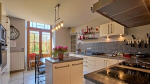A modern kitchen with white cabinets, a central island, and a built-in stove. - CAPE - maison avec piscine et jacuzzi (Thénac)