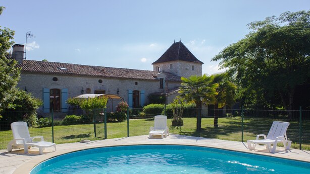A swimming pool with lounge chairs, a stone building with a tower, and a fenced garden area. - CAPE - maison avec piscine et jacuzzi (Thénac)
