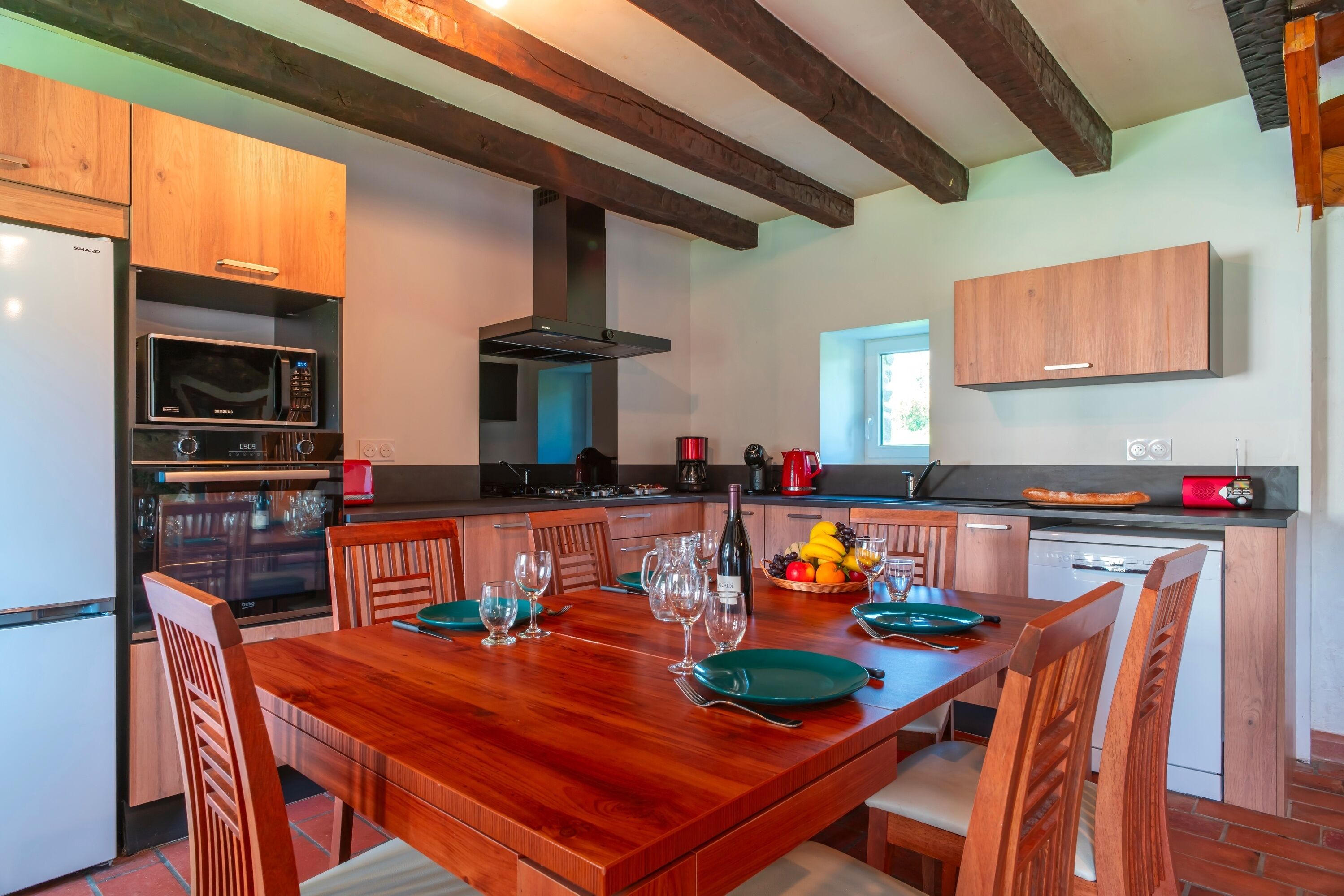 Una cocina moderna con armarios de madera, horno empotrado, microondas y un gran comedor preparado para seis personas.