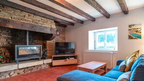 Una sala de estar con chimenea de piedra, un televisor de pantalla plana, una mesa de centro de madera y un sofá azul.