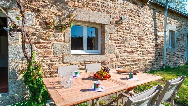 Un edificio de piedra con una mesa y sillas de madera, una ventana y una cesta de frutas.