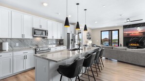 A modern kitchen with white cabinets, a large island with bar stools, and a dining area with a gray sofa.
