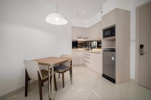 A modern kitchen with a dining table and chairs, a microwave, and a refrigerator. - Cassia Residences, One Bedroom A Deluxe Lake (Choeng Thale)