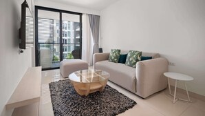 Una sala de estar moderna con un sofá, una mesa de centro de vidrio, una mesita auxiliar y un ventanal grande con cortinas.