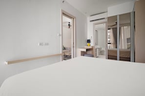 A hotel room with a large bed, a desk, a chair, and a wardrobe.