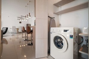 A modern laundry room with a front-loading washing machine, a sink, and a chair. - Cassia Residences, Three-Bedroom B Premium Lake (Choeng Thale)
