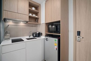 Una cocina compacta con armarios blancos, un refrigerador negro, un microondas y un horno empotrado.