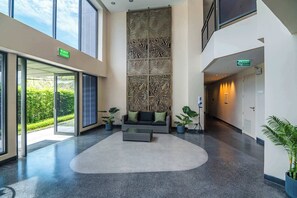 Un vestíbulo con un amplio panel decorativo, un sofá con cojines, plantas en macetas y una señal de salida.