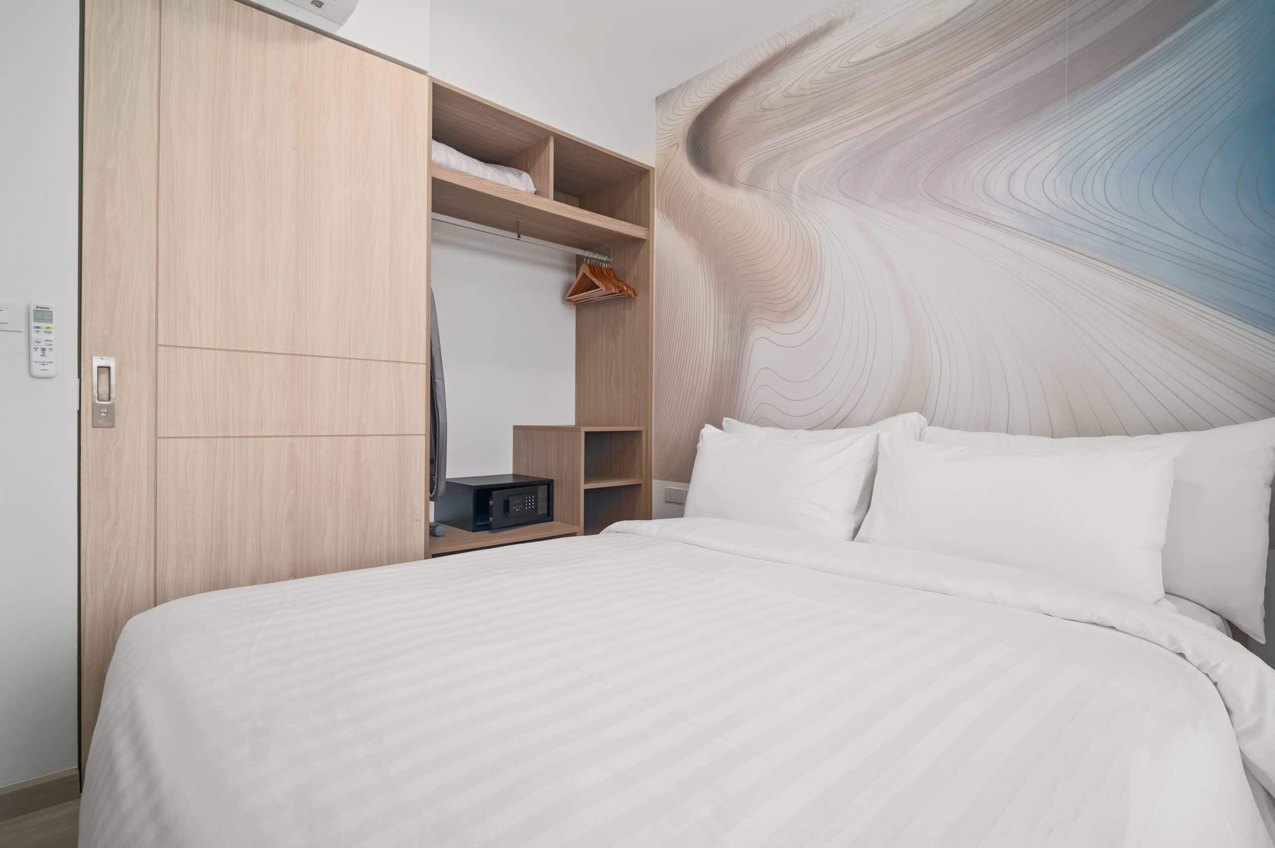 Een hotelkamer met een groot bed, een kledingkast met meerdere planken en een muur met een abstract, spiraalvormig ontwerp.