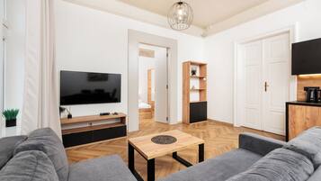 Un salon moderne doté d’un téléviseur à écran plat, de canapés gris, d’une table basse en bois et d’un parquet à motifs en chevrons.