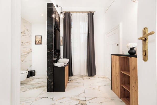 Un baño moderno con suelo de mármol, tocador negro, inodoro blanco y cortina de ducha.