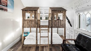 Una habitación con cama tipo litera, una escalera, un sofá de cuero negro y una ventana con vistas.