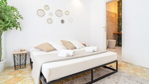 A modern bedroom with a bed, a potted plant, a bedside table, and a bathroom visible through an open door. - Home Sicily suite (Pachino)