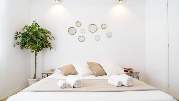 A neatly made bed with white and beige bedding, a potted plant, and a wall with circular wall art. - Home Sicily suite (Pachino)