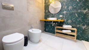 A modern bathroom with a toilet, bidet, sink, and a shelf with towels. - Home Sicily suite (Pachino)