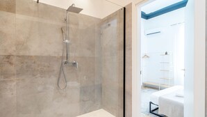 A modern bathroom with a glass-enclosed shower, a white bathtub, and a small bedside table with a plant. - Home Sicily suite (Pachino)