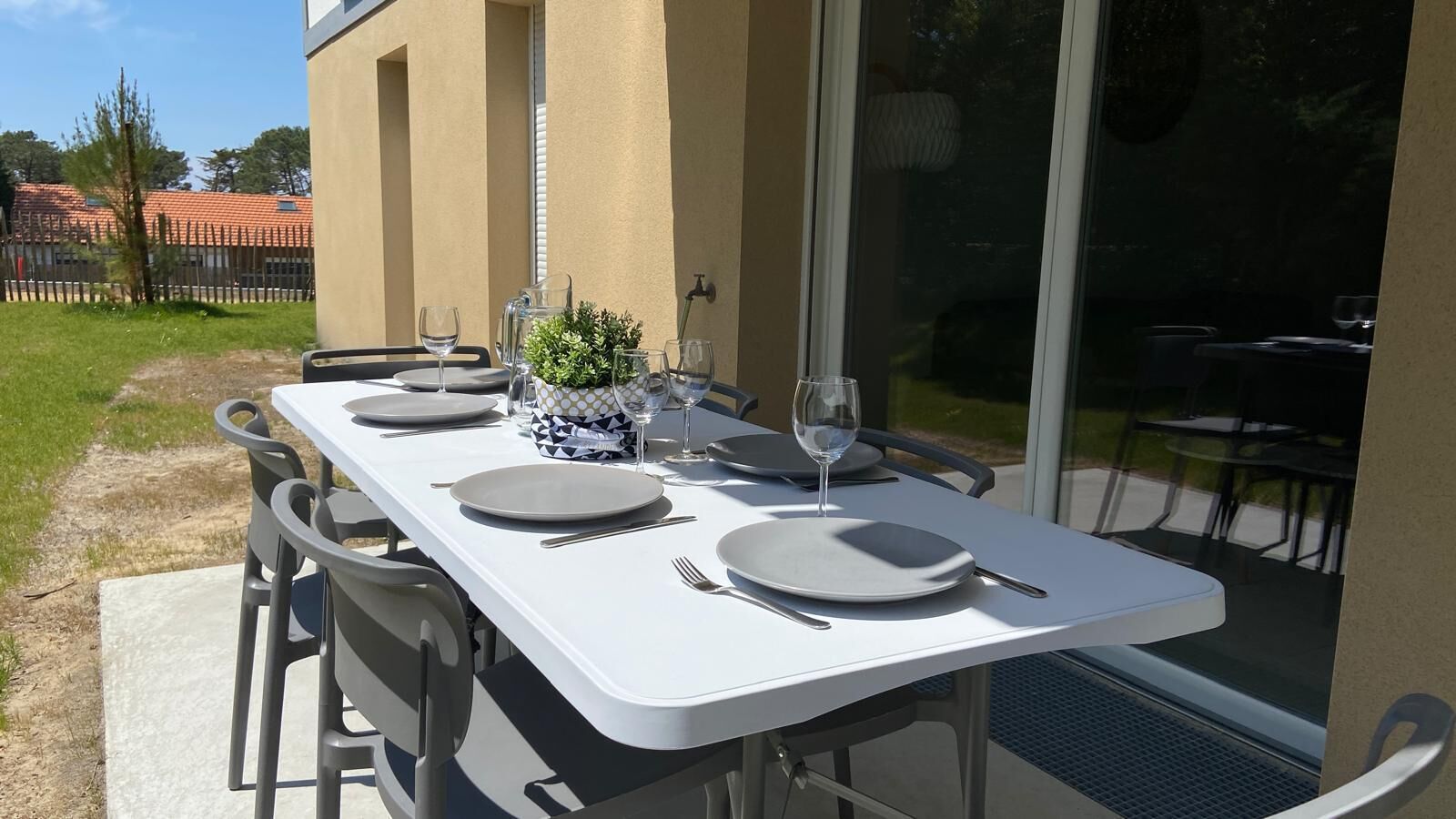 Un área de comedor al aire libre con una mesa blanca preparada para cuatro personas, rodeada de sillas.