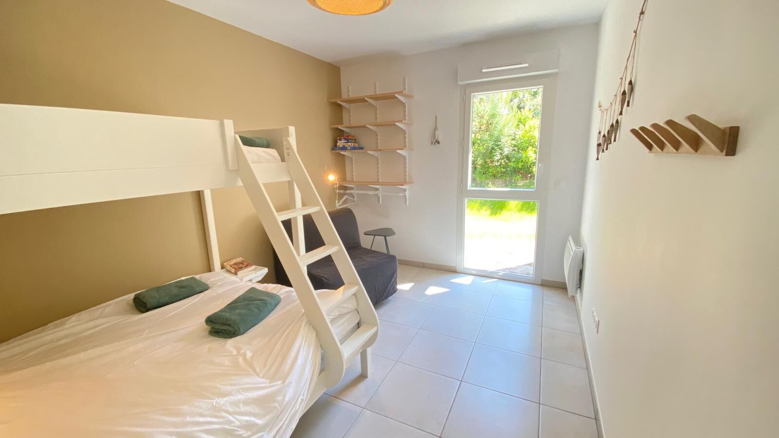 A bedroom with a bunk bed, a desk, a chair, and a window with a view of greenery.