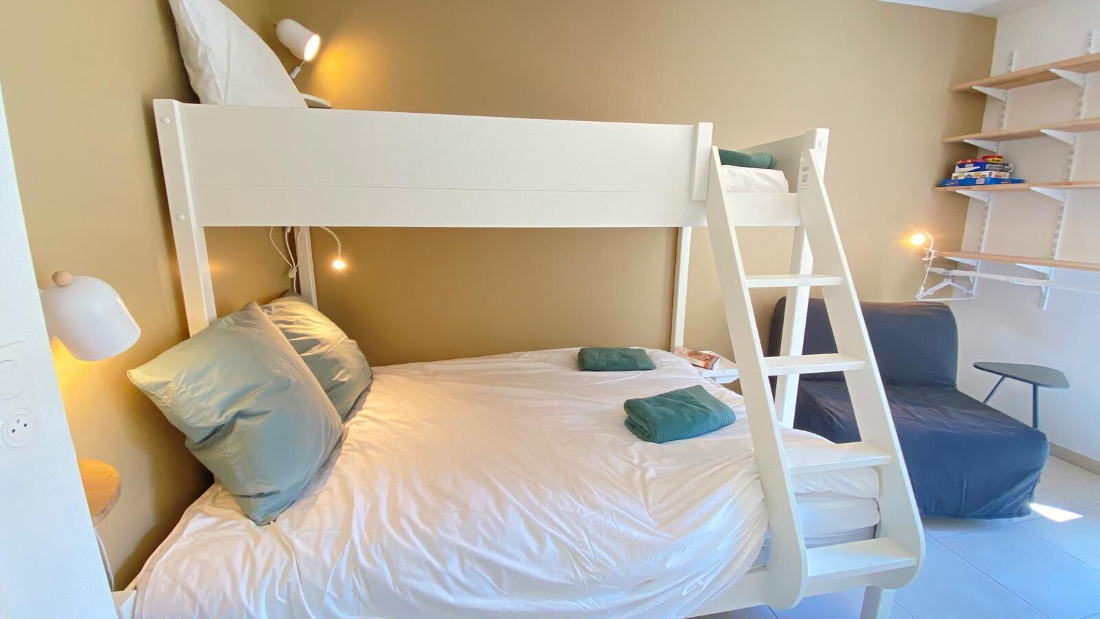Una cama litera con escalera, un escritorio y estantes en una habitación con paredes color beige.
