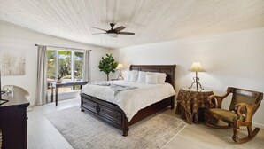 A bedroom with a wooden ceiling fan, a large bed with a white comforter, two bedside lamps, a rocking chair, and a small table with a lamp. - Club Ironwood Resort Access, Desert Garden & Golf (Carefree)