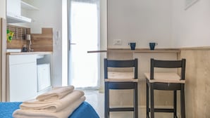 Habitación de hotel con cama, dos sillas, una mesita, ventana y kitchenette.
