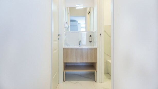 Un pasillo estrecho que conduce a un baño con un lavamanos blanco, espejo y un perchero.