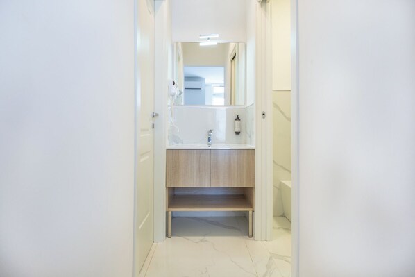 Un pasillo estrecho que conduce a un baño con un lavamanos blanco, espejo y un perchero.