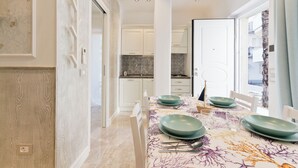 A dining area with a table set for four, white cabinets, and a view of the kitchen in the background.