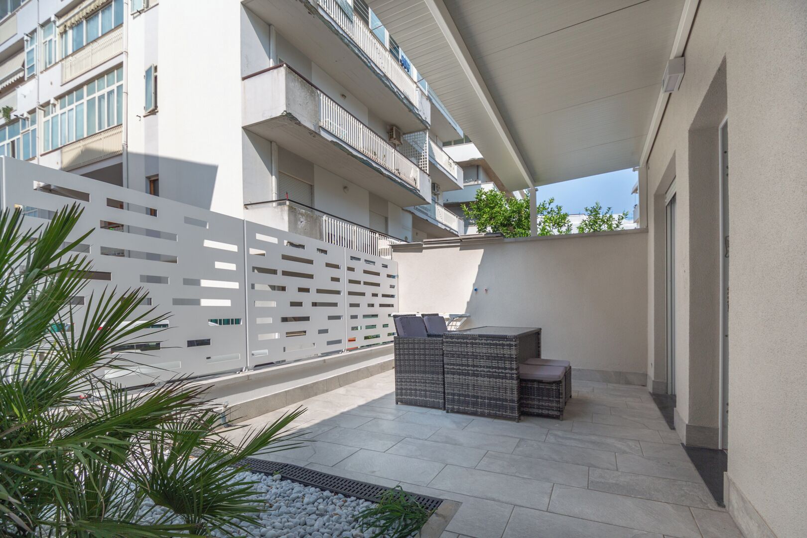 A modern outdoor patio with a seating area, a white fence, and a building in the background.