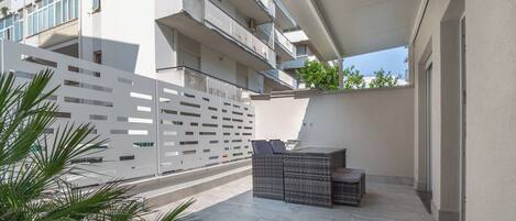 A modern outdoor patio with a seating area, a white fence, and a building in the background.