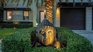 Une statue de Bouddha dans un jardin, avec un bâtiment en arrière-plan.