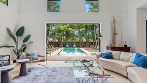 Un salon moderne avec une piscine, un canapé en cuir, une table basse en verre et une grande fenêtre donnant sur un jardin tropical.