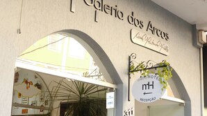 The entrance to a hotel with a sign reading "Galeria dos Arcos" and "Hotel Metropol." There is a reception desk and a potted plant near the entrance. - Metro Hotel (Aguas de Lindoia)