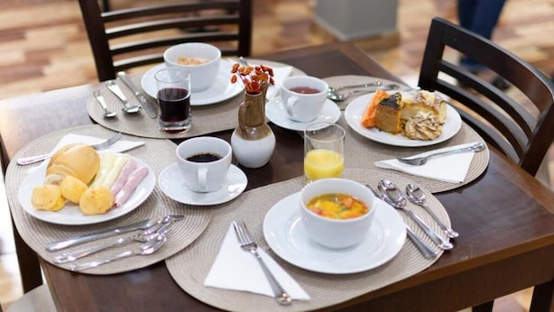 A breakfast table set with plates of food, cups, and cutlery. - Metro Hotel (Aguas de Lindoia)