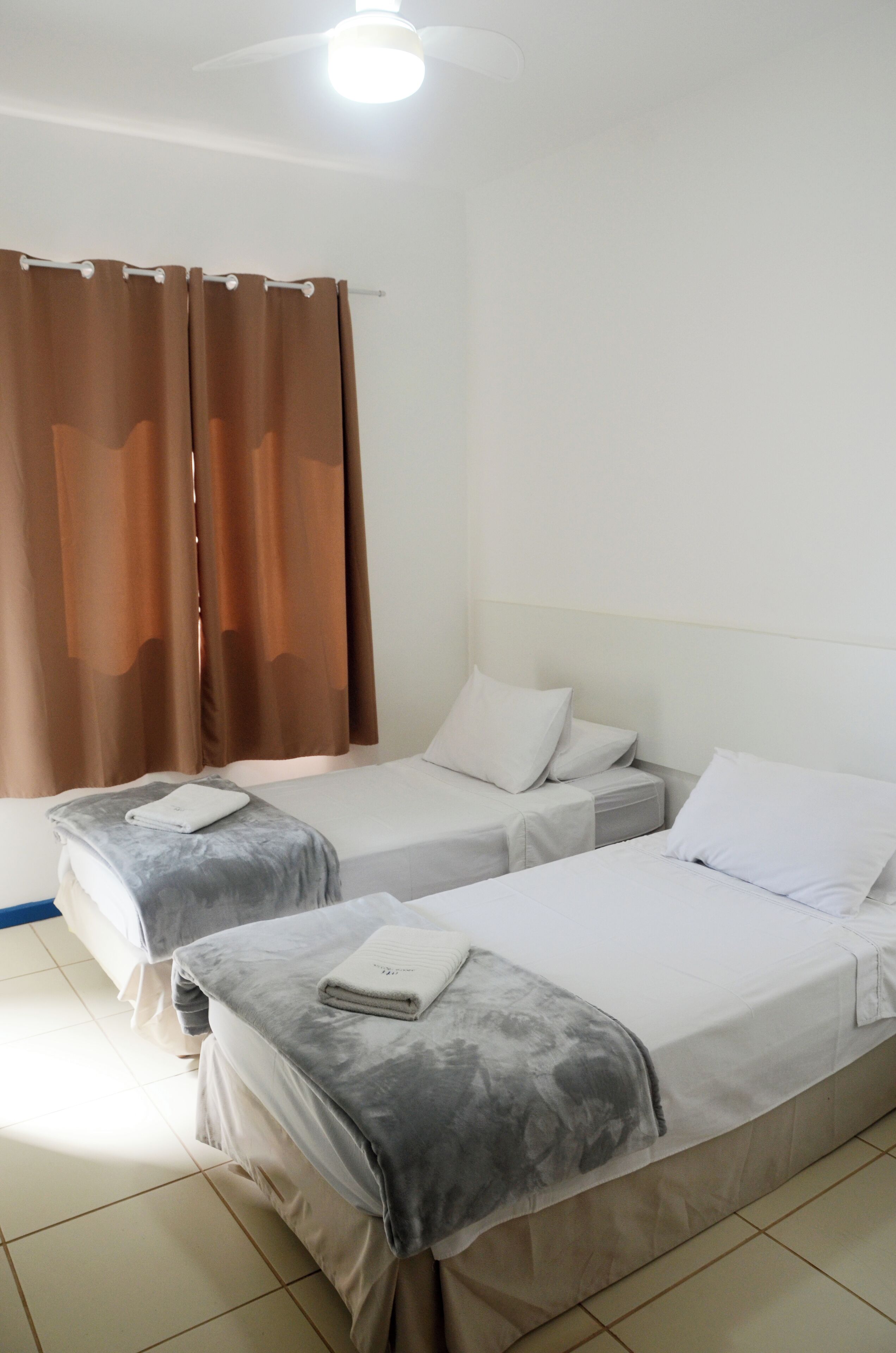 A hotel room with two single beds, a small table, a chair, and a window with curtains.