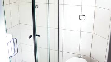 Une salle de bain avec une douche à parois de verre, des toilettes blanches et une poubelle.
