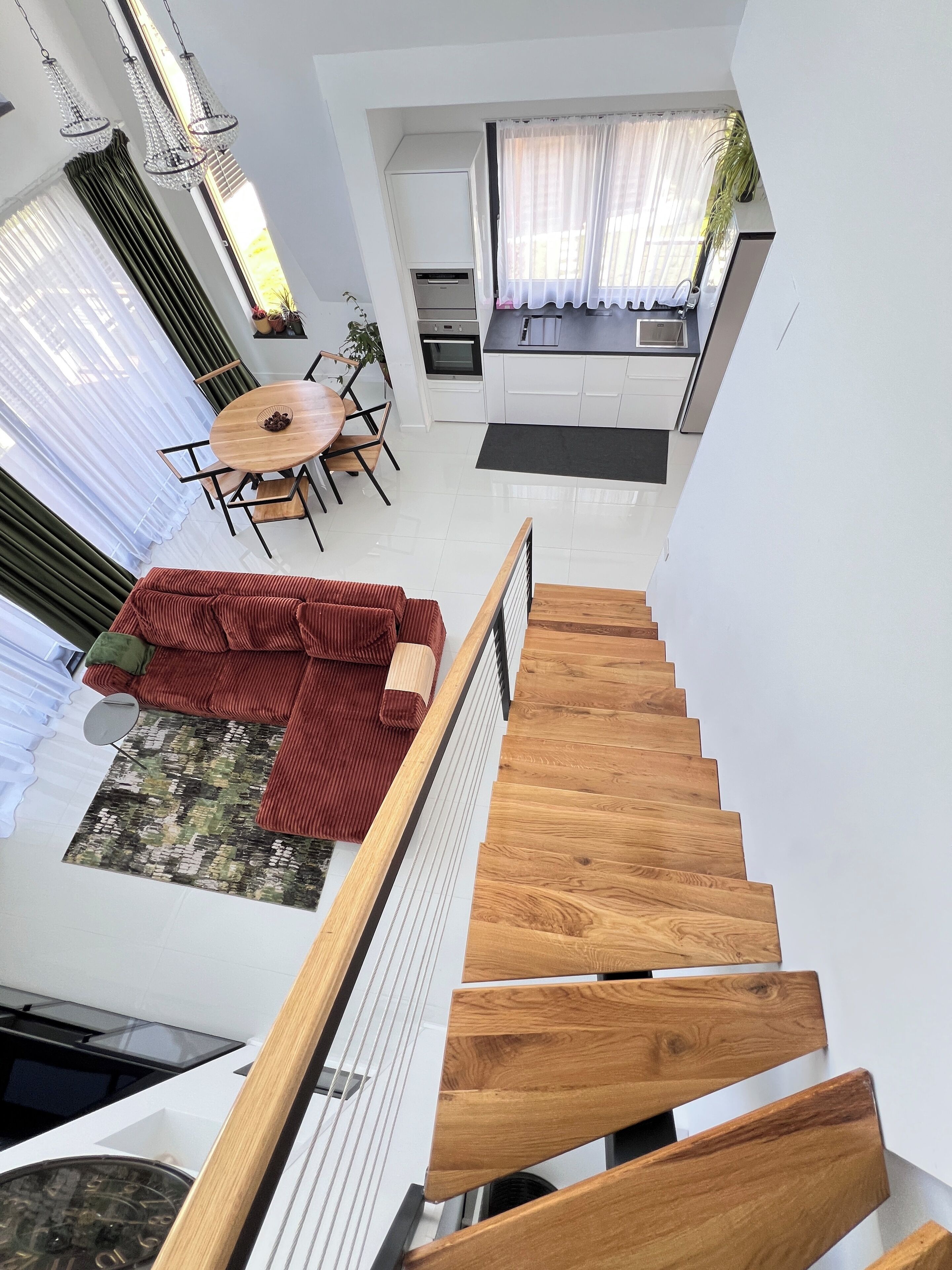 A modern interior with a wooden staircase, a dining area with a round table, and a kitchen with white cabinets.