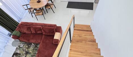 A modern interior with a wooden staircase, a dining area with a round table, and a kitchen with white cabinets.