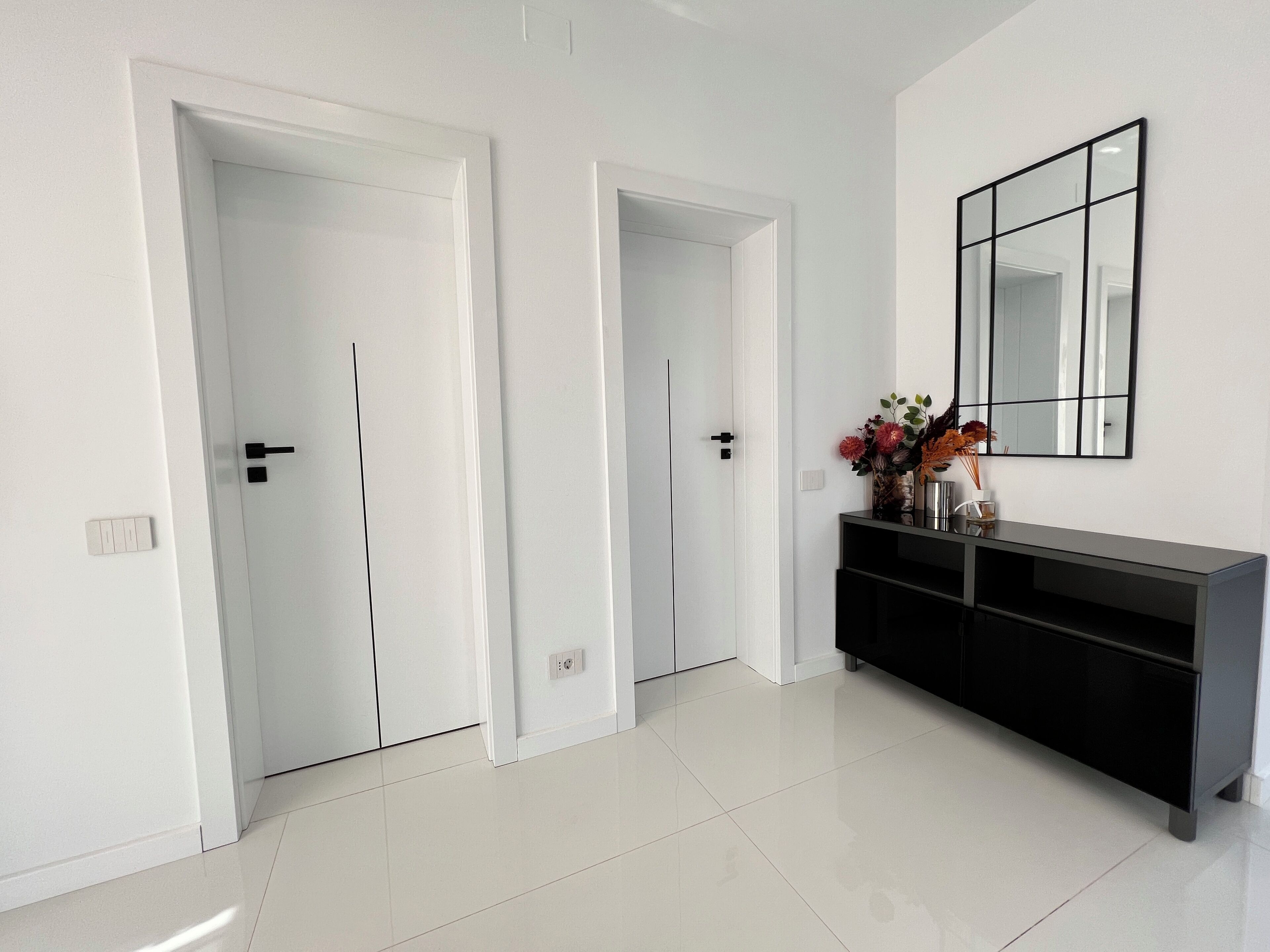 A hallway with white doors, a black console table, and a large mirror on the wall.